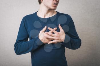 Man hurt heart, hands on his chest. Gray background.