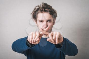 Man showing X fingers. Gray background.