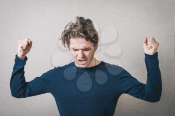 Man angry, shouts, lifting his hands up into fists. Gray background