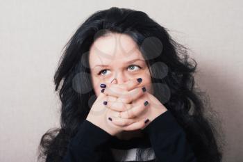 Woman with long hair covering her face with her hands. Gray background