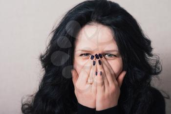 Woman with long hair covering her face with her hands. Gray background