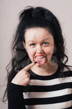 Woman shows a finger on the tongue. Gray background.
