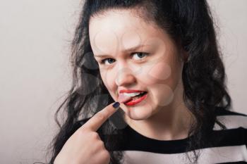 Woman shows a finger on the tongue. Gray background.
