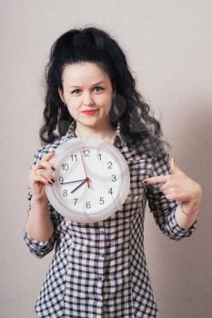 Woman showing  a wall clock. On a gray background.