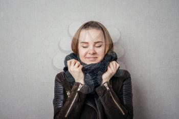 It is so cold. Frozen young women covering face with turtleneck while standing against grey background
