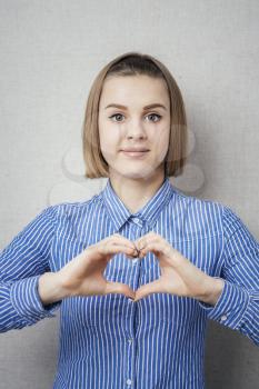 beautiful young blond woman making a heart gesture with her fingers