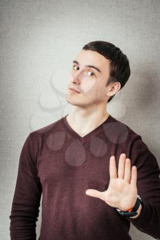 portrait of young man doing stop symbol over grey background