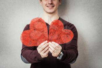 A young man holding two a red heart in his hands