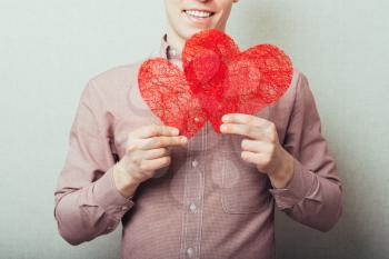 A young man holding two red hearts in hands