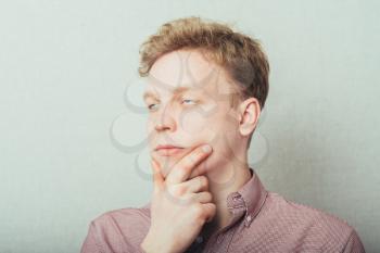 Portrait of the young thinking man looks up with hand near face