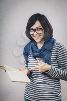 young woman smiles and shows finger in book.