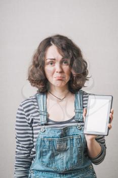 Girl holding a mobile tablet and upset, dressed in overalls
