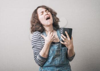 Girl holding a mobile tablet and upset, dressed in overalls