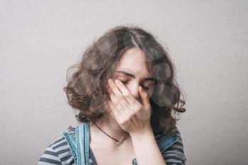 Girl upset and covers her face with her hands, rear view dressed in overalls