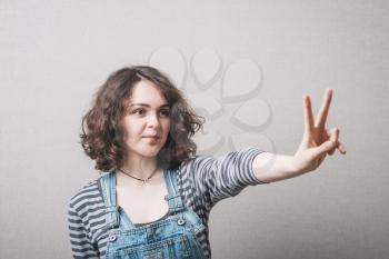 A woman makes a gesture of victory. Gray background