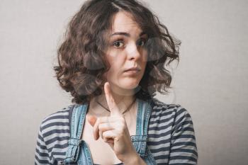 Woman shows up the index finger, gently attention. Gray background
