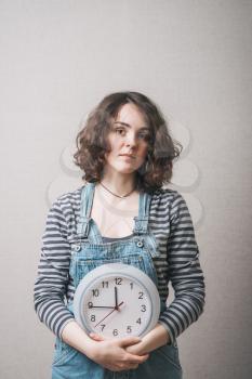 A woman is holding a large clock. Gray background