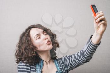 Woman playfully makes selfie on the phone, a grimace. Gray background