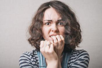 Woman bites his nails on the experiences of fear. On a gray background.