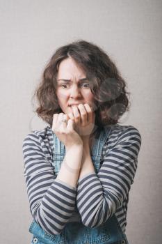 Woman bites his nails on the experiences of fear. On a gray background.