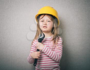 beautiful little girl in helmet with wrench isolated on gray background