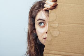 girl looks out from behind a cardboard paper