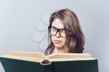 girl with glasses reading a book, looking from her