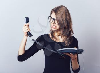 Woman with the office or home phone swears, screams. On a gray background.