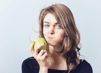 Beautiful young woman bites a green apple on a gray background
