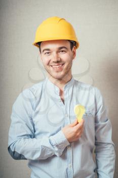 A man in a yellow helmet holding a sticker in the form of light bulbs on a gray background.