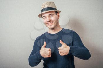 A man in a hat shows thumbs up. On a gray background.