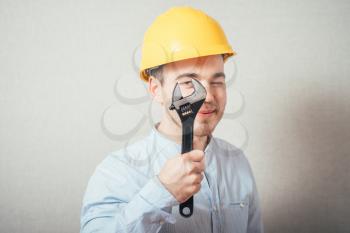The man in yellow helmet looking through a wrench. On a gray background.