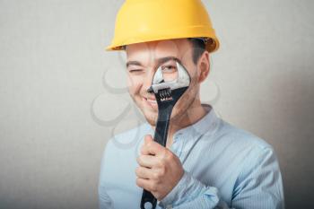 The man in yellow helmet looking through a wrench. On a gray background.