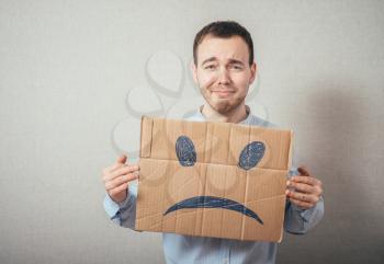 Young man with an unhappy smiley card half covering face