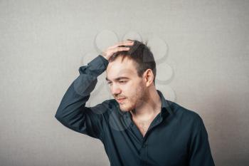 Man thinks upset with his hand near his head. On a gray background.
