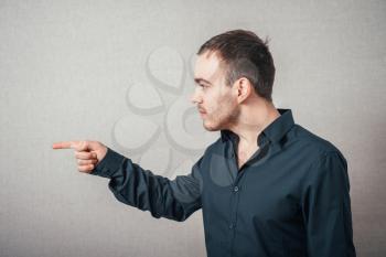 Man shows a finger forward, profile. On a gray background.
