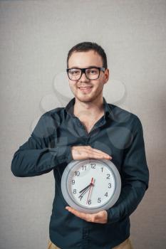 A man holding a wall clock. On a gray background.