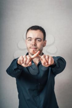 A man shows the hands stop timeout, fingers X. On a gray background.