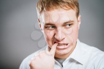 Closeup portrait of man biting his thumb fingernail or finger in mouth, very stressed and nervous, isolated on gray background with copy space