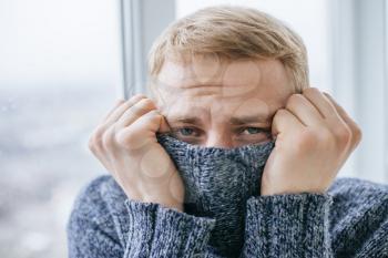 Young man feeling cold in flat near the window