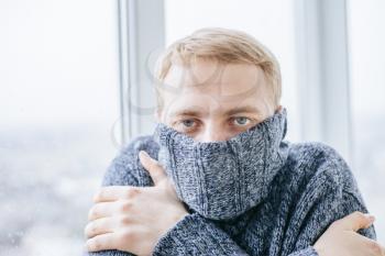 Young man feeling cold in flat near the window