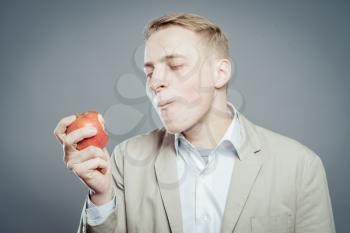 Cheerful beautiful man eating apple, isolated over gray background