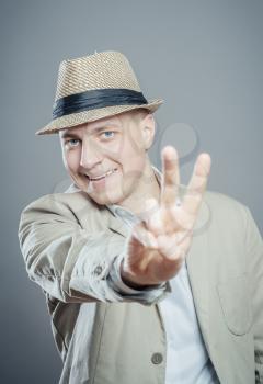 Portrait of a charming young man in hat showing you victory sign
