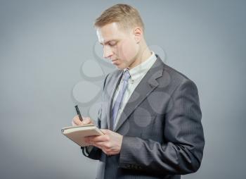 Businessman in suit writing on empty notepad (notebook)