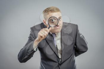 Funny image of a adult man with a magnifying glass, one eye is enlarged.