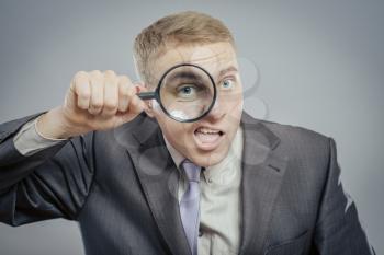 Funny image of a adult man with a magnifying glass, one eye is enlarged.