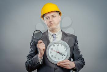 engineer man in helmet with a magnifying glass and big clock, it's time to inspection