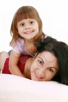 A portrait of a mother and her baby girl lying on the bed and smiling over white background 
