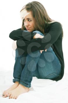 Sad girl teenager sits twining arms about legs. Isolated on a white background. 
