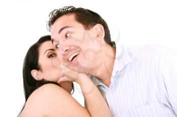 pretty girl talking secret to young man in his ear, man smiling over isolated white background 